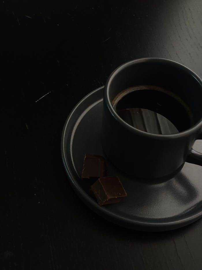 A dark coffee in a stylish cup with chocolate squares on a matching saucer.